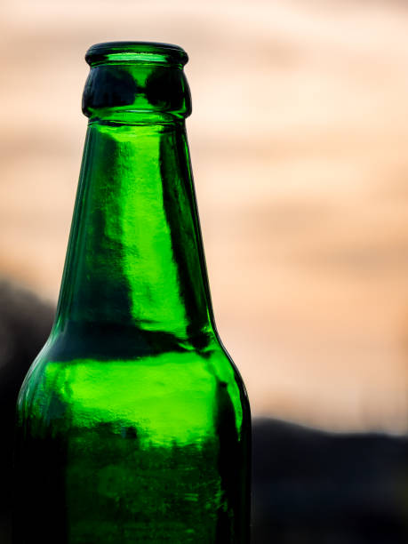 empty green beer bottle neck stands in relief against the evening sky, capturing the essence of twilight and the relaxation that follows the workday, epitomizing the joy of unwinding with a cold brew. - refundable imagens e fotografias de stock