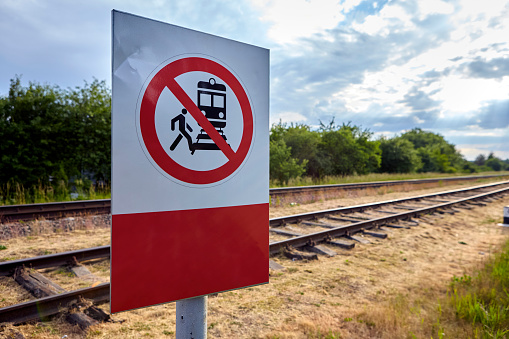 A concrete railway track under a sunny sky with a vivid prohibition sign displaying a train and a person, emphasizing no crossing. The scene captures rail safety on a lovely day.