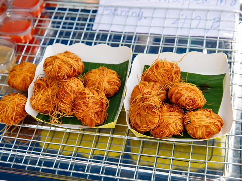 Deep Fried Pork Balls Wrap in rice Egg Noodles (Moo Sa Rong or Sarong) lying on banana leaves and paper plate on street food market tray, Thai Traditional fast Food, close up, top view