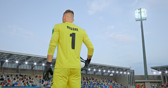 Low angle view of male goalkeeper in yellow jersey standing on football pitch during match.