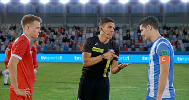 Referee showing coin to team captions during toss on football pitch.