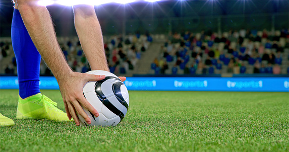 Close-up of male football player adjusting ball on grass during match.