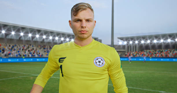 Portrait of male goalkeeper in yellow jersey standing on football pitch during match.