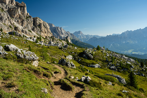 Trail in the Dolomites Mountains with green trees and mountains in the background in the summer at cloudless sky and warm day