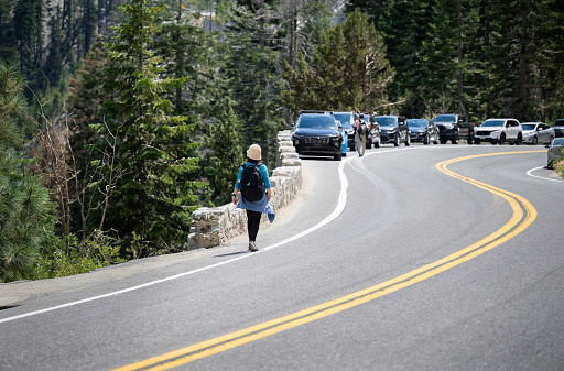 People walking on the side of busy Emerald Bay Road. Cars parked along the road. Lake Tahoe. California.