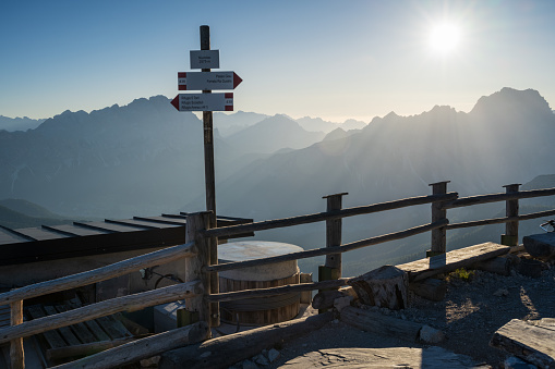 Sunrise at Nuvolau near rifugio with guidepost and sunrays over rocky mountains in background