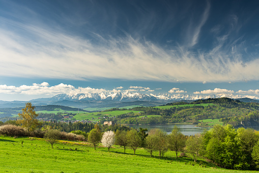 Spring panorama with green fields and trees in Malopolska region, Poland. Czorsztyn castle and snow covered Tatra Mountains behind, Pieniny and beautiful clouds on blue sky.