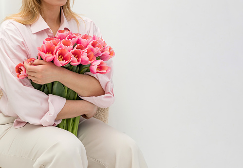 Girl in pink shirt and light colored pants holding a large bouquet of pink tulips. Copy space