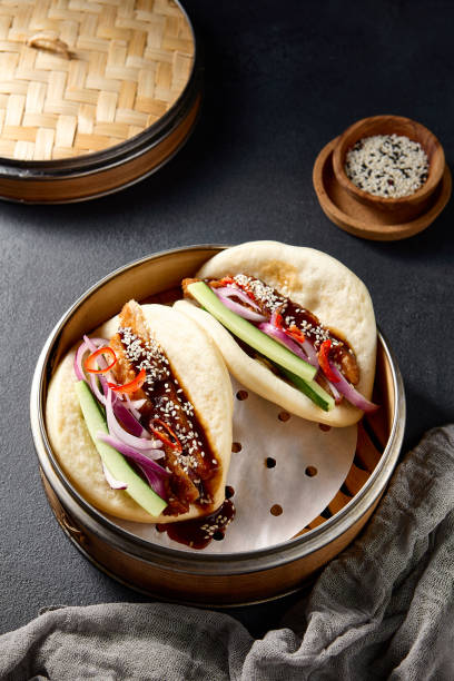 istock Authentic Asian cuisine: Bao buns with duck and vegetables in a steamer on a black table 2101204674