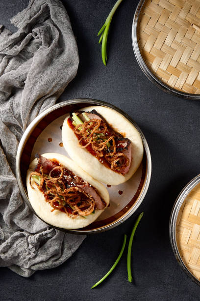 istock Top view of gourmet Bao buns with roast beef and crispy onion strings on a black background 2101204676