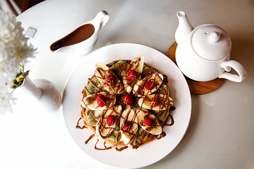 A white plate is filled with mouth-watering waffles, topped with a delectable assortment of toppings.