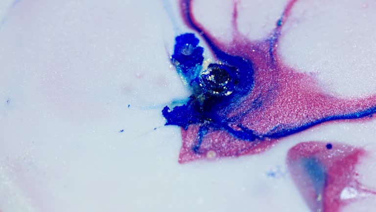 Vibrant blue and pink inks spreading in water with a glittery effect, close-up