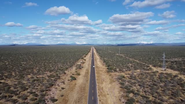 A straight road with a white car cutting through the vast desert of baja california sur, aerial view