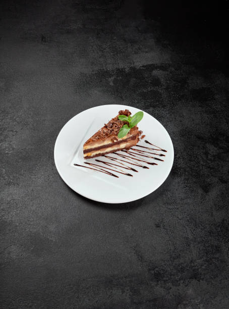 istock Peanut and caramel cake with chocolate topped on white plate on dark stone background. Piece of Snickers cake in minimal style. Toffee, nuts and chocolate cake in confectionery menu. 2101243977
