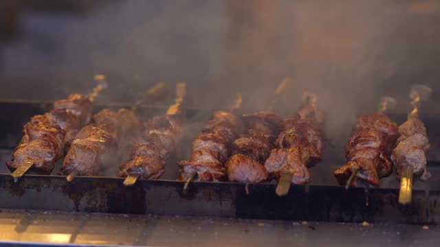 Juicy delicious barbecue is fried on hot coals on the grill. It rotates on a spit around its axis. Food festival Fried juicy meat on skewers. Pork meat is fried on coals.