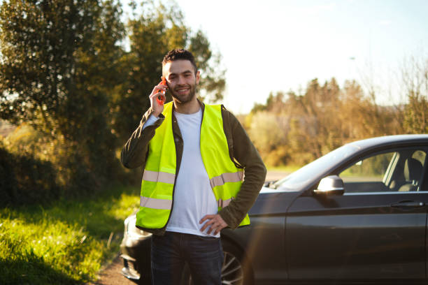 istock Man smiling while talking to the mobile next to broken car in a rural road 2101283256