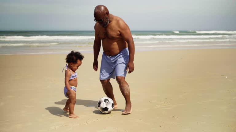 Dad and his cute baby daughter playing ball on the beach