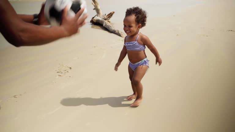 Dad and his cute baby daughter playing ball on the beach