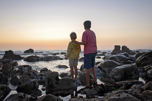 Happy children, enjoying sunset over the ocean with their family, rocky beach in Portugal
