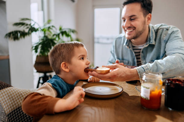 istock Father feeding his son with jam sandwich at home 2101305596