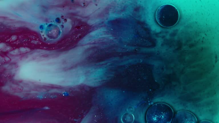 Colorful ink clouding in water creating an abstract art effect, with vibrant turquoise and magenta hues merging