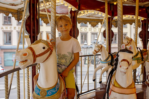 Children, boys, going on Merry Go Round, kids play on carousel summertime in Strasbourg, France during summer vacation