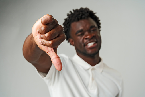 Young African Man Giving Thumbs Down Gesture Against a Neutral Background in Studio