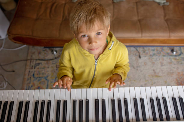 Child, blond boy, playing piano at home, learning