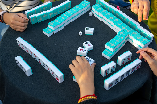 A group of friends engrossed in a strategic game of Mahjong, focusing intently on their hands and tiles as they immerse themselves in the ancient Chinese tradition