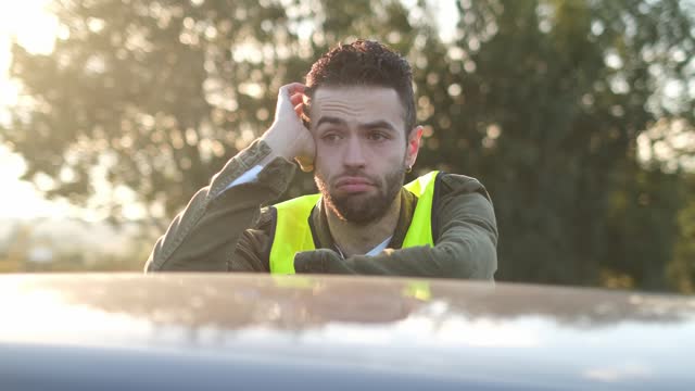 Frustrated man waiting for road assistance leaning on a broken car