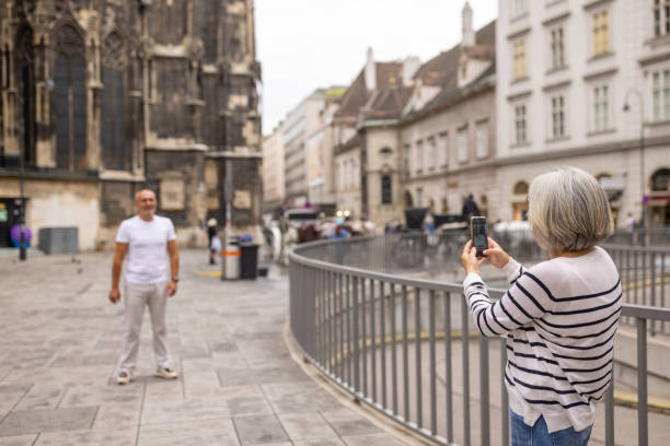 Wife photographing her husband with smart phone in front of cathedral in beautiful Vienna.