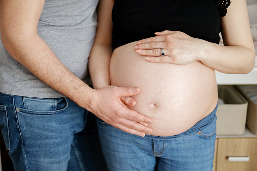 Part of an unrecognizable man touching the belly of a pregnant woman