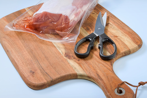 The vacuum packaging of the meat with on table with scissors. Take out the piece of meat from the plastic vacuum packaging.