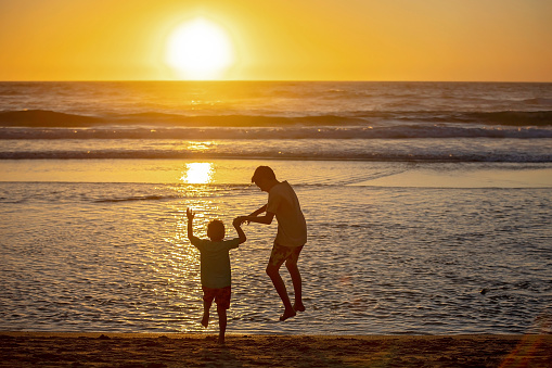 Child playing on ocean beach. Kid jumping in the waves at sunset. Sea vacation for family with kids. Little boy and girl running on exotic island during summer holiday.