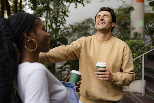 Cheerful male student laughing while spending time with his black girlfriend on the street.