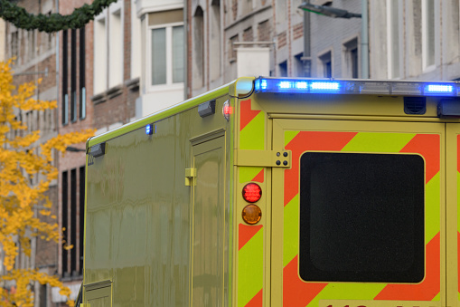 An ambulance on a city street, a fragment of the corps with the light signal on.