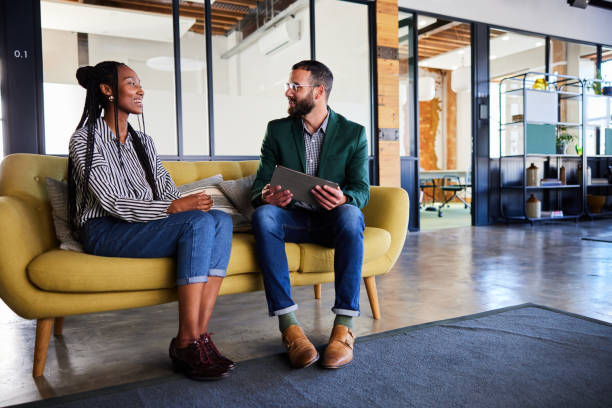 Two smiling young businesspeople talking and working on a tablet in an office
