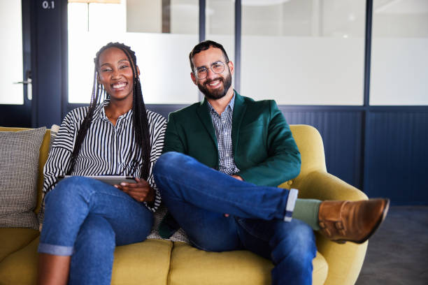 istock Two smiling young businesspeople using a tablet on a sofa in an office lounge 2101366802