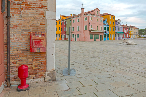 Venice, Italy - January 10, 2017: Red Fire Hydrant and Post Box at Brick Wall Colourful Houses Town Square in Burano Island Winter Day Travel.