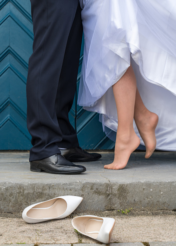 Wedding details. A wedding couple against a background of blue gates. Only the feet of the young couple, the bride stands without shoes, wedding shoes lie next to her
