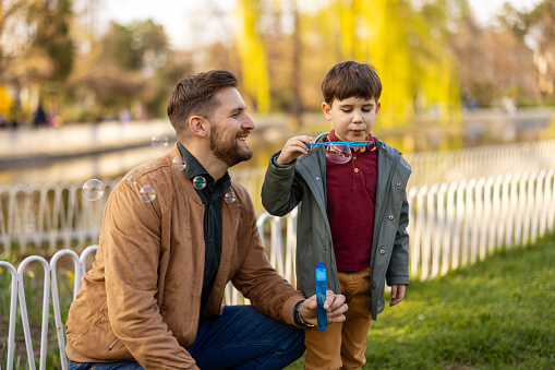 I love you, dad! Handsome young man with his little cute boy are having fun and blowing soap bubbles outdoors