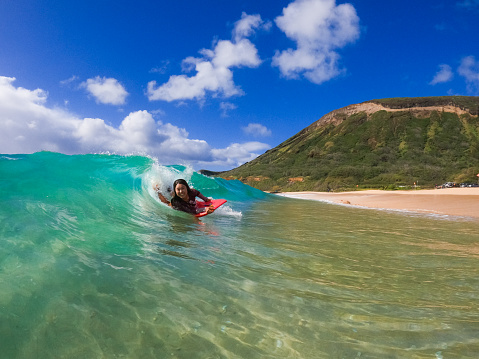 A young tanned Japanese woman happily riding a wave in Hawaii.