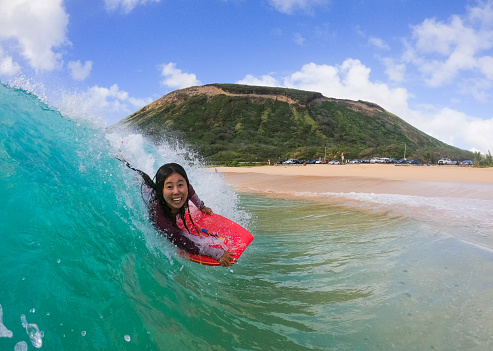 A young tanned Japanese woman happily riding a wave in Hawaii.