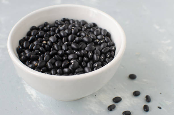 Raw black bens in a white bowl on a gray background. Concept of healthy eating. Vegetarian and vegan food. Horizontal orientation. Selective focus stock photo