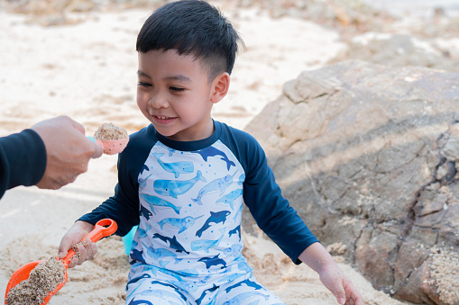 Gorgeous little boy and dad have fun digging in the sand at the beach. Selective focus.