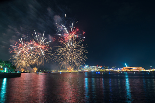 A stunning display of fireworks with vibrant colors lighting up the night sky, reflected over the calm waters of a city's waterfront area of Yas Island waterfront in Abu Dhabi UAE. Fireworks displays in the UAE typically occur during major events and celebrations such as New Year's Eve, National Day, Eid holidays, Expo events, and other special occasions.