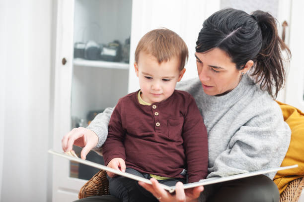Smiling mother reading a book to her son while relaxing together on a comfortable sofa at home