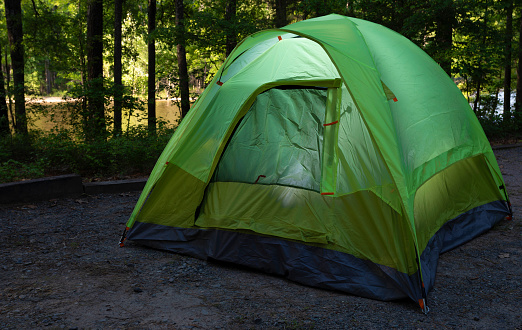 Two man backpacking tent at a campsite with lights on inside and lake in sunlight behind.
