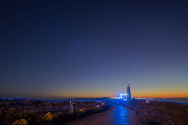Path to the cross on a stone pillar at Cabo da Roca with fire truck with blue lights under the night sky, Sintra, Lisbon, Portugal
