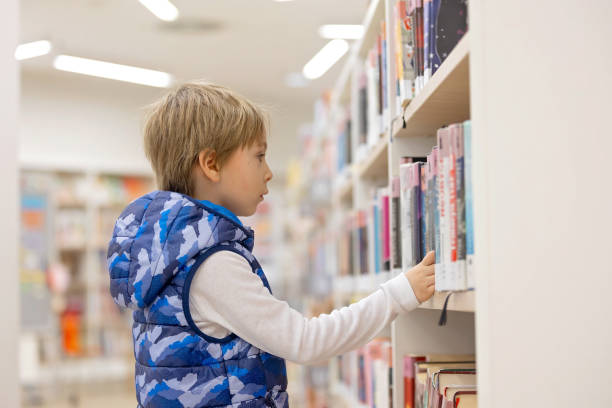 istock Smart child, school boy, educating himself in a library, borrowing books 2101513395